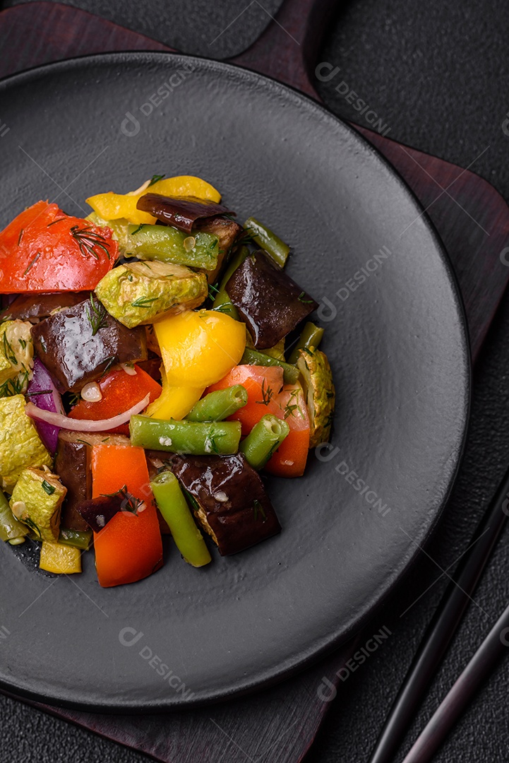 Deliciosa salada fresca e suculenta de berinjela assada, tomate, abobrinha, cebola, especiarias e sal sobre um fundo escuro de concreto