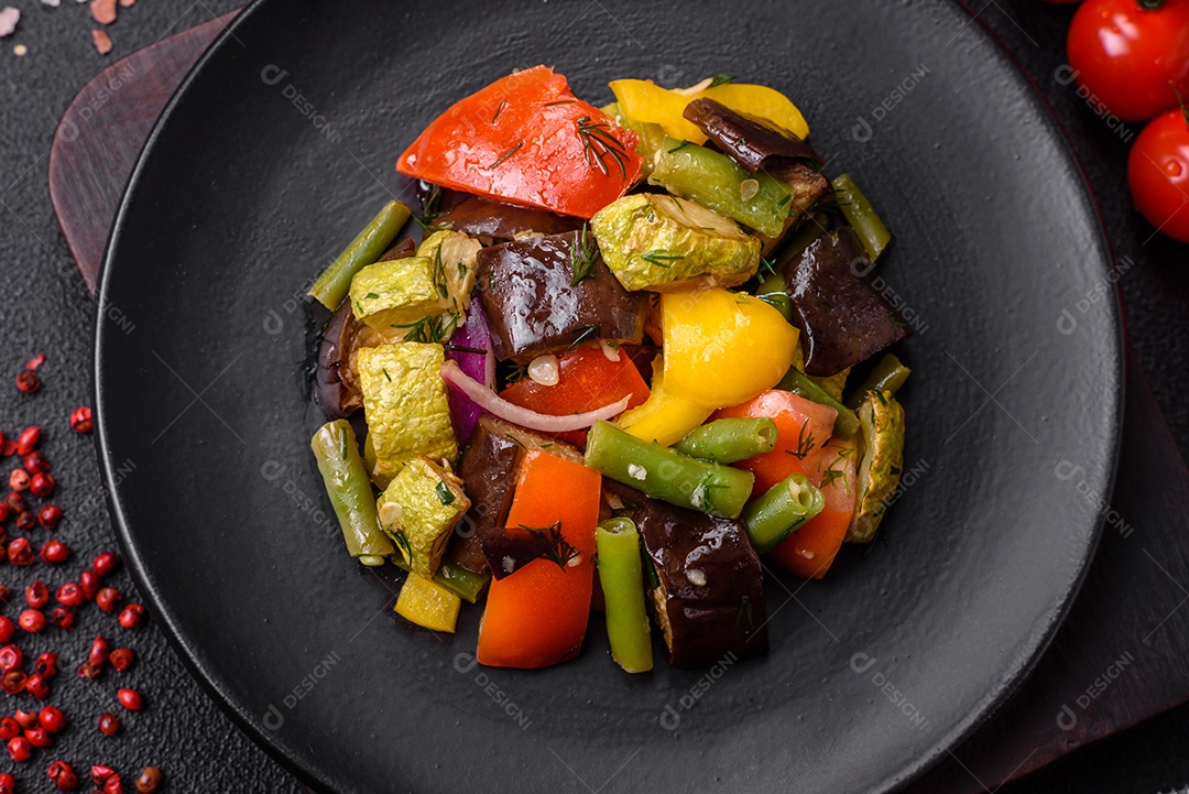 Deliciosa salada fresca e suculenta de berinjela assada, tomate, abobrinha, cebola, especiarias e sal sobre um fundo escuro de concreto