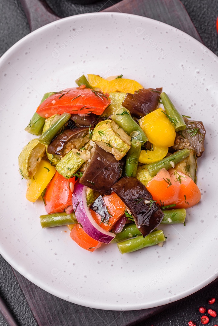 Deliciosa salada fresca e suculenta de berinjela assada, tomate, abobrinha, cebola, especiarias e sal sobre um fundo escuro de concreto