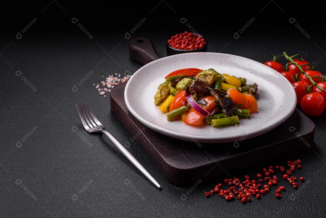 Deliciosa salada fresca e suculenta de berinjela assada, tomate, abobrinha, cebola, especiarias e sal sobre um fundo escuro de concreto