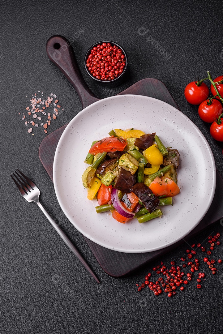 Deliciosa salada fresca e suculenta de berinjela assada, tomate, pimentão, sementes de gergelim, especiarias e sal sobre um fundo escuro de concreto