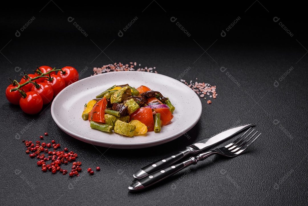Deliciosa salada fresca e suculenta de berinjela assada, tomate, pimentão, sementes de gergelim, especiarias e sal sobre um fundo escuro de concreto