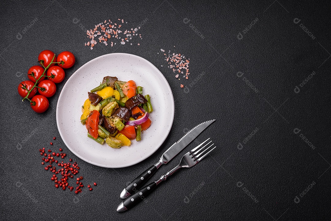 Deliciosa salada fresca e suculenta de berinjela assada, tomate, pimentão, sementes de gergelim, especiarias e sal sobre um fundo escuro de concreto