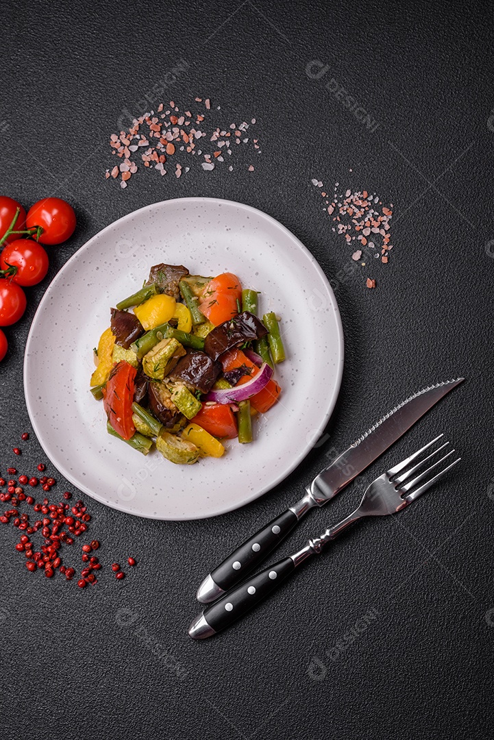 Deliciosa salada fresca e suculenta de berinjela assada, tomate, pimentão, sementes de gergelim, especiarias e sal sobre um fundo escuro de concreto