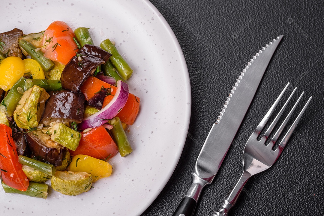 Deliciosa salada fresca e suculenta de berinjela assada, tomate, pimentão, sementes de gergelim, especiarias e sal sobre um fundo escuro de concreto