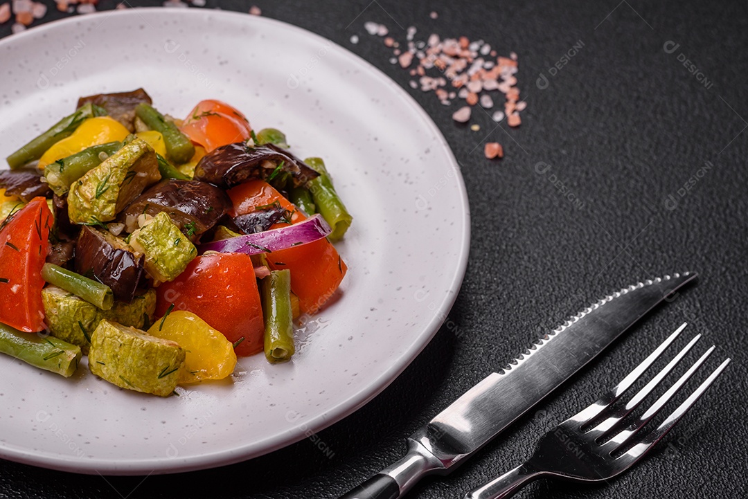 Deliciosa salada fresca e suculenta de berinjela assada, tomate, pimentão, sementes de gergelim, especiarias e sal sobre um fundo escuro de concreto
