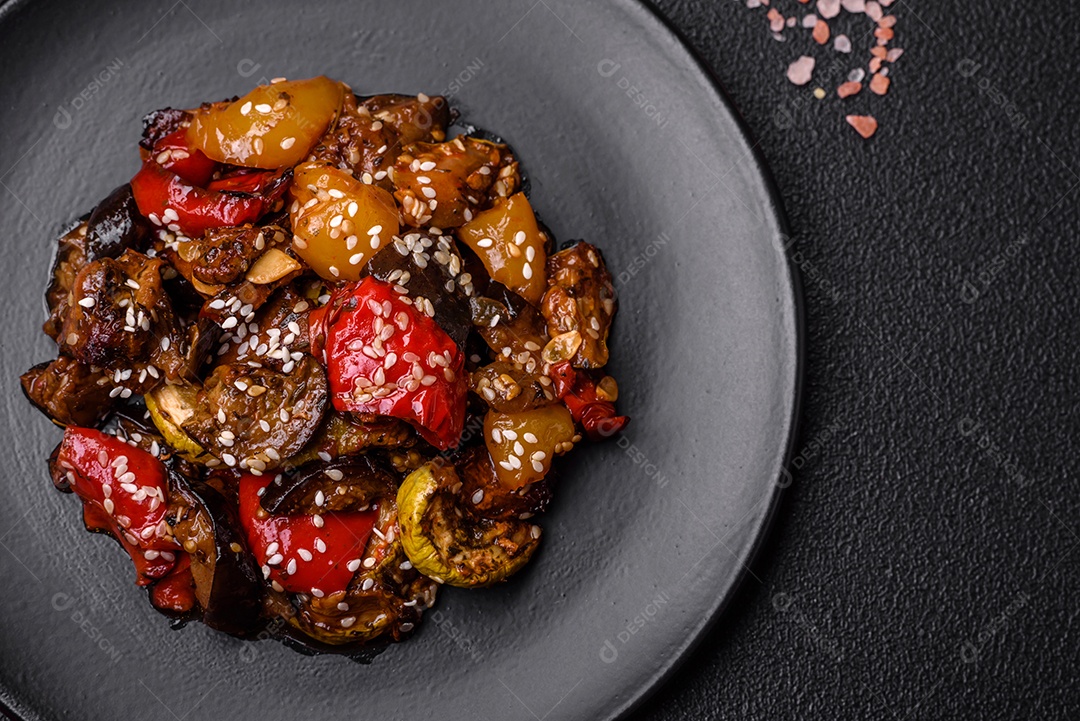 Deliciosa salada fresca e suculenta de berinjela assada, tomate, pimentão, sementes de gergelim, especiarias e sal sobre um fundo escuro de concreto
