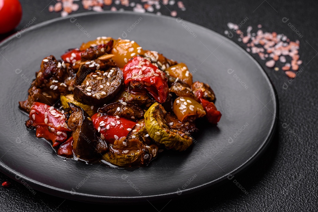 Deliciosa salada fresca e suculenta de berinjela assada, tomate, pimentão, sementes de gergelim, especiarias e sal sobre um fundo escuro de concreto