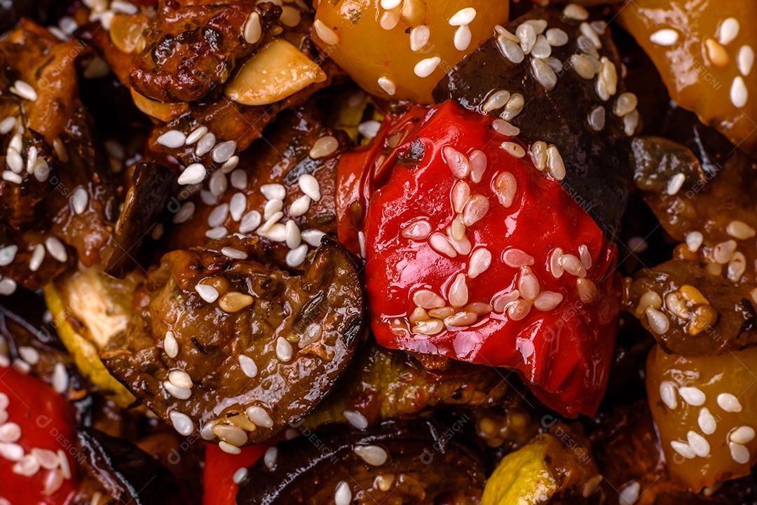 Deliciosa salada fresca e suculenta de berinjela assada, tomate, pimentão, sementes de gergelim, especiarias e sal sobre um fundo escuro de concreto