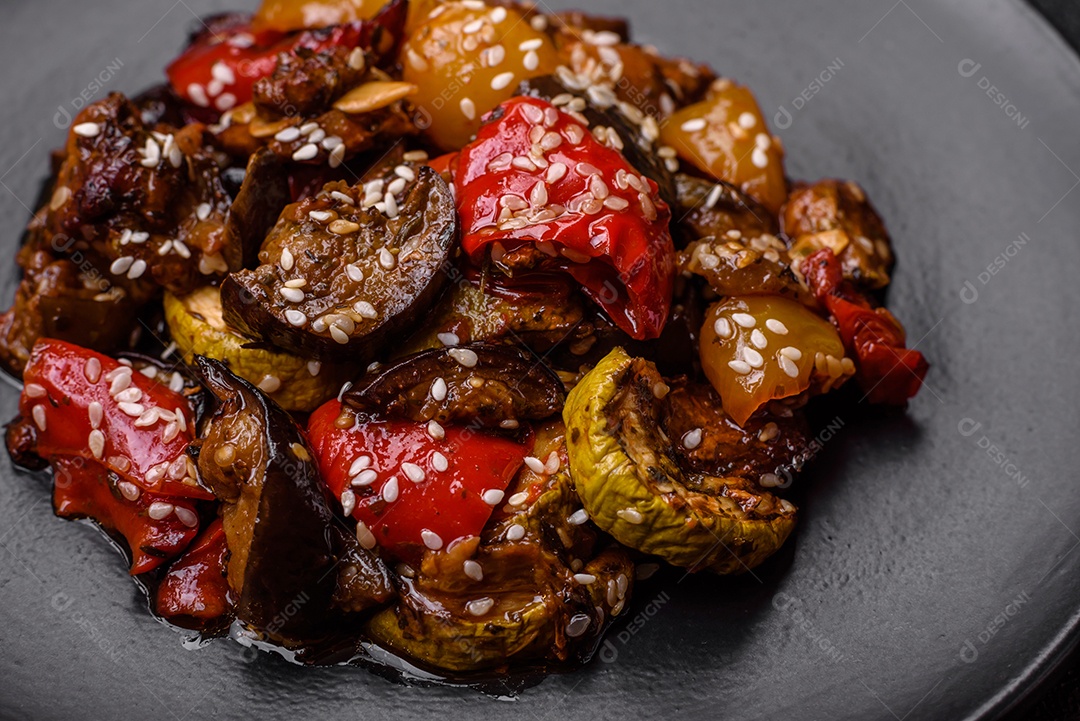 Deliciosa salada fresca e suculenta de berinjela assada, tomate, pimentão, sementes de gergelim, especiarias e sal sobre um fundo escuro de concreto