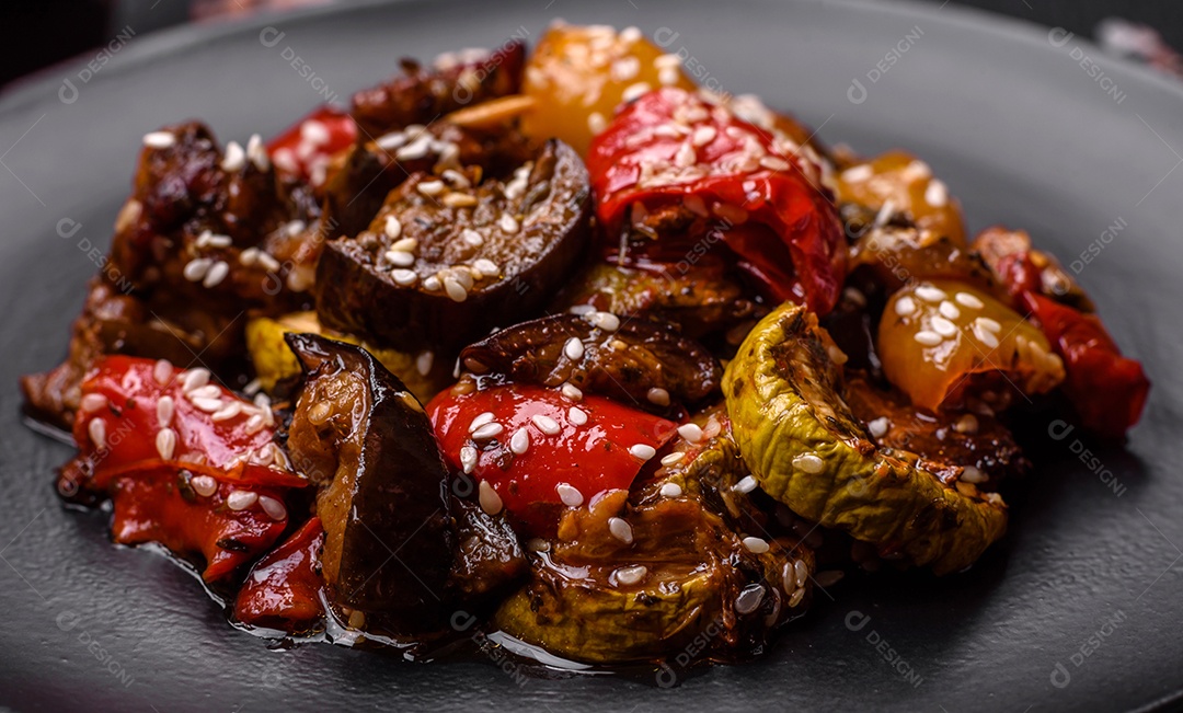 Deliciosa salada fresca e suculenta de berinjela assada, tomate, pimentão, sementes de gergelim, especiarias e sal sobre um fundo escuro de concreto