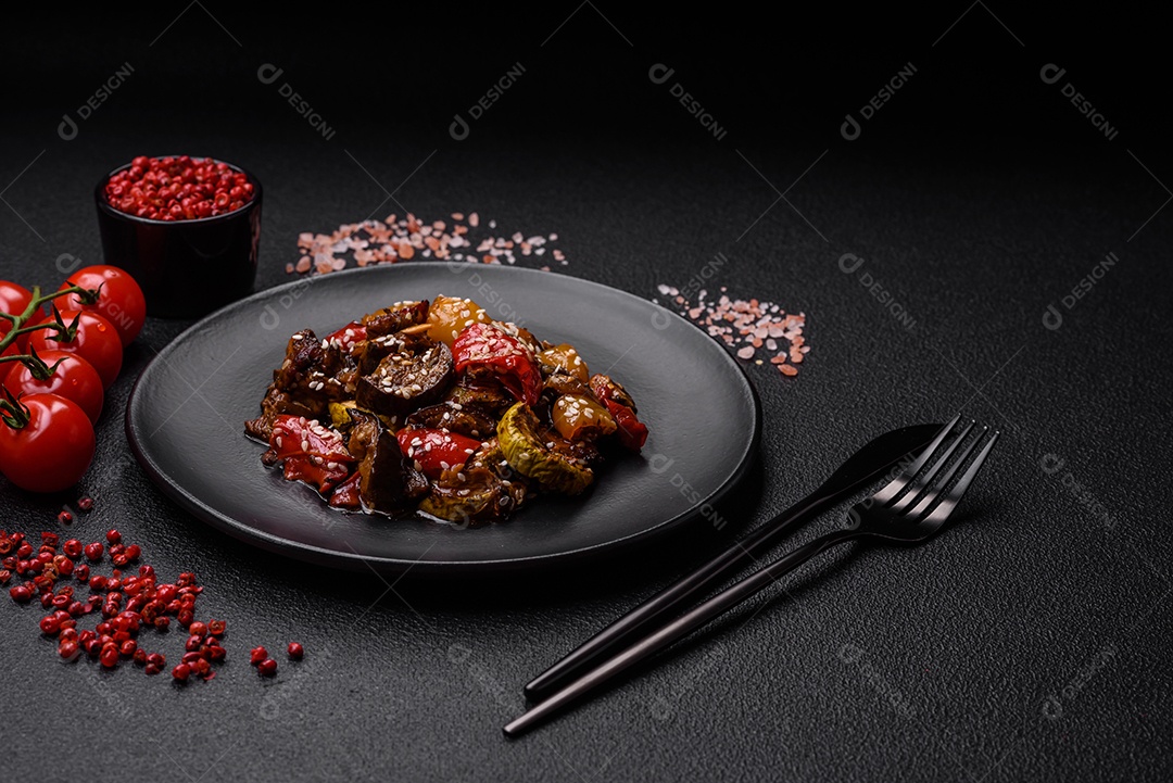 Deliciosa salada fresca e suculenta de berinjela assada, tomate, pimentão, sementes de gergelim, especiarias e sal sobre um fundo escuro de concreto