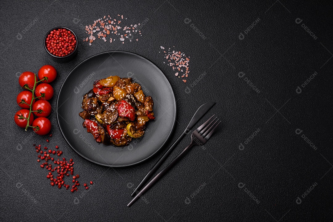 Deliciosa salada fresca e suculenta de berinjela assada, tomate, pimentão, sementes de gergelim, especiarias e sal sobre um fundo escuro de concreto
