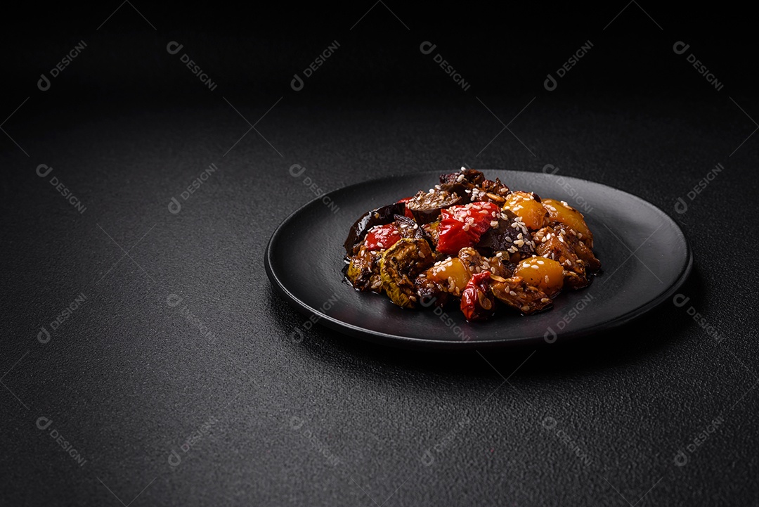Deliciosa salada fresca e suculenta de berinjela assada, tomate, pimentão, sementes de gergelim, especiarias e sal sobre um fundo escuro de concreto