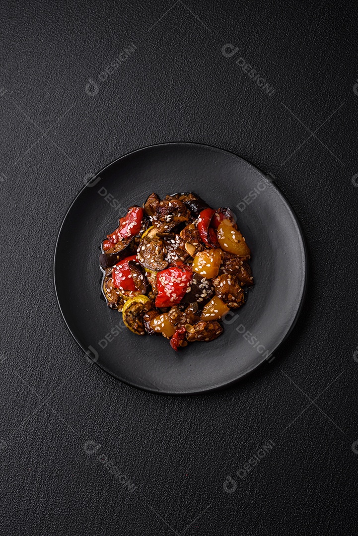 Deliciosa salada fresca e suculenta de berinjela assada, tomate, pimentão, sementes de gergelim, especiarias e sal sobre um fundo escuro de concreto