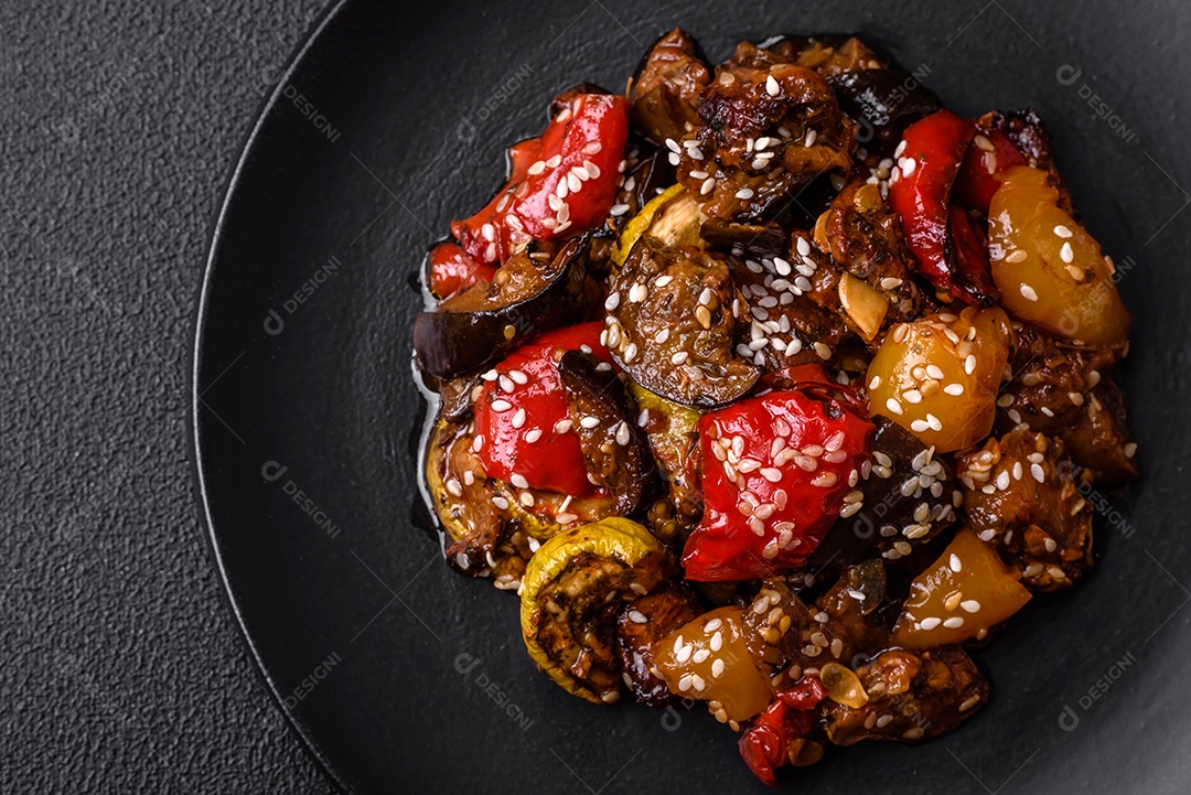 Deliciosa salada fresca e suculenta de berinjela assada, tomate, pimentão, sementes de gergelim, especiarias e sal sobre um fundo escuro de concreto