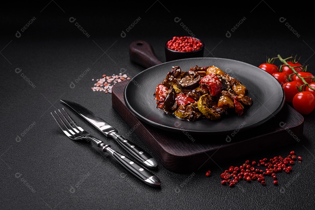 Deliciosa salada fresca e suculenta de berinjela assada, tomate, pimentão, sementes de gergelim, especiarias e sal sobre um fundo escuro de concreto