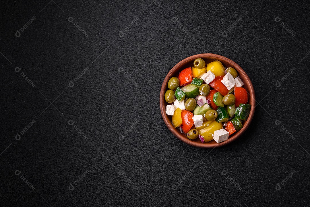 Deliciosa salada grega fresca e suculenta com queijo feta, azeitonas, tomates, pepino, pimenta, sal e especiarias sobre um fundo escuro de concreto