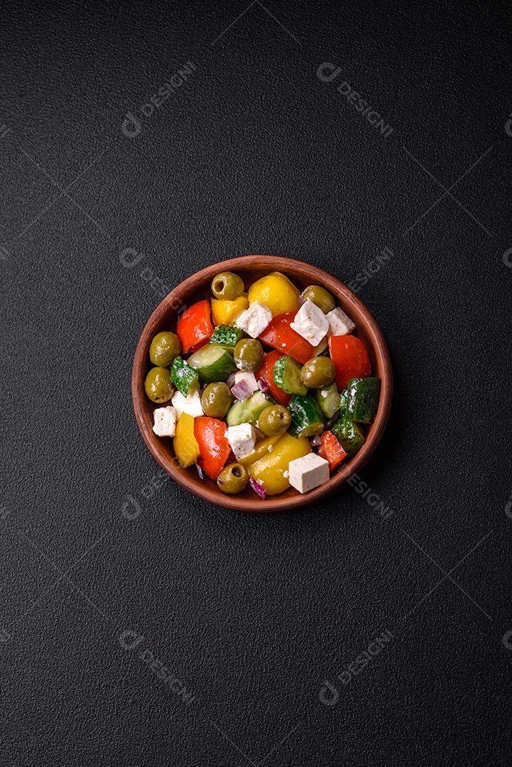 Deliciosa salada grega fresca e suculenta com queijo feta, azeitonas, tomates, pepino, pimenta, sal e especiarias sobre um fundo escuro de concreto
