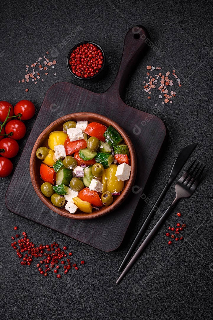 Deliciosa salada grega fresca e suculenta com queijo feta, azeitonas, tomates, pepino, pimenta, sal e especiarias sobre um fundo escuro de concreto