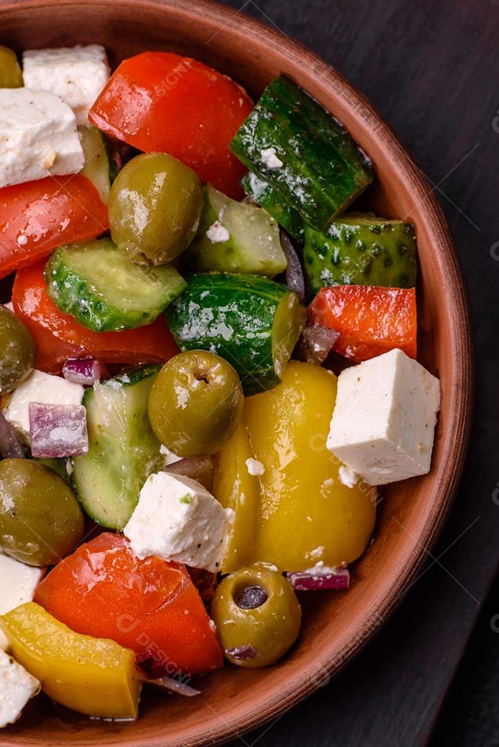 Deliciosa salada grega fresca e suculenta com queijo feta, azeitonas, tomates, pepino, pimenta, sal e especiarias sobre um fundo escuro de concreto