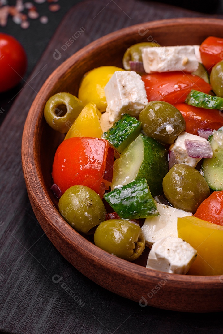 Deliciosa salada grega fresca e suculenta com queijo feta, azeitonas, tomates, pepino, pimenta, sal e especiarias sobre um fundo escuro de concreto