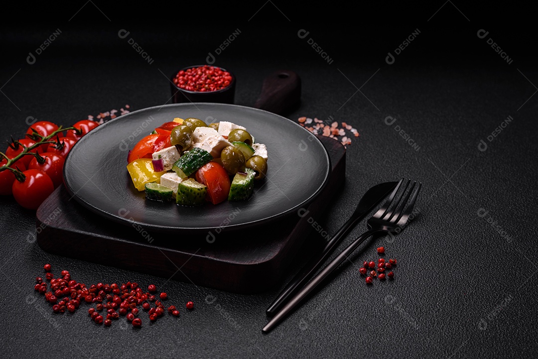 Deliciosa salada grega fresca e suculenta com queijo feta, azeitonas, tomates, pepino, pimenta, sal e especiarias sobre um fundo escuro de concreto