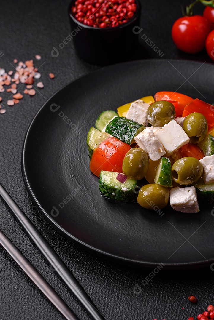 Deliciosa salada grega fresca e suculenta com queijo feta, azeitonas, tomates, pepino, pimenta, sal e especiarias sobre um fundo escuro de concreto
