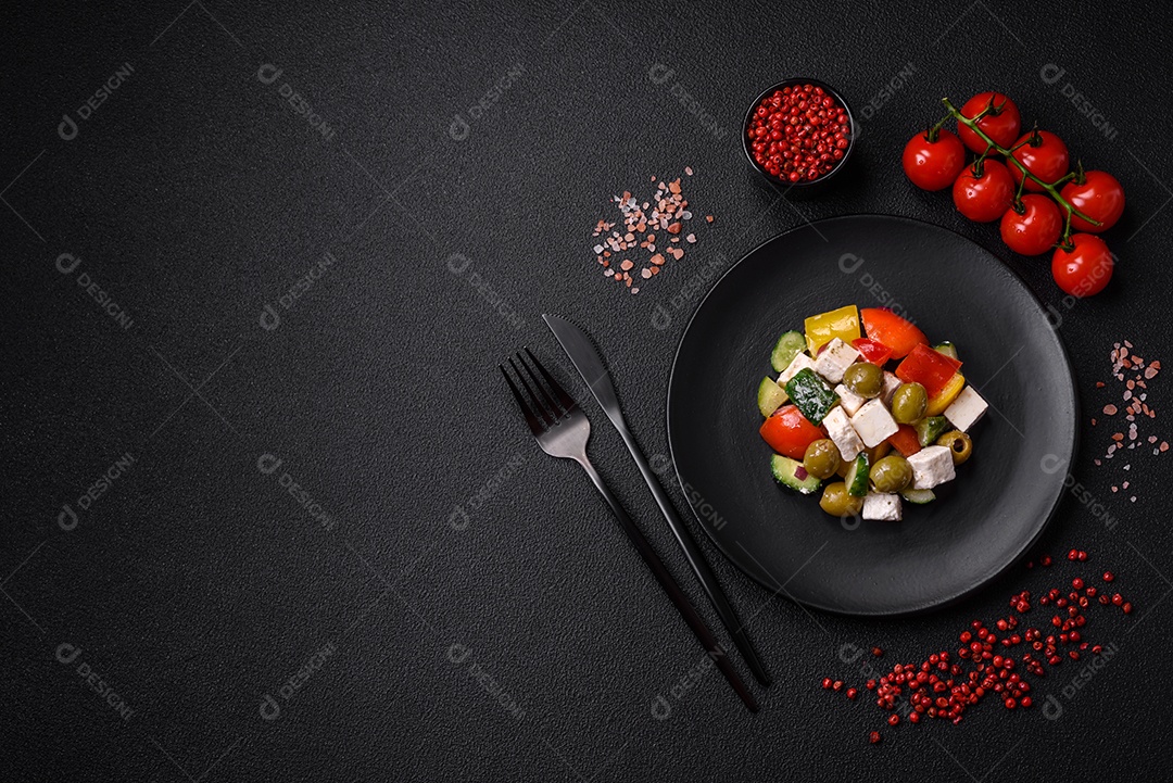 Deliciosa salada grega fresca e suculenta com queijo feta, azeitonas, tomates, pepino, pimenta, sal e especiarias sobre um fundo escuro de concreto