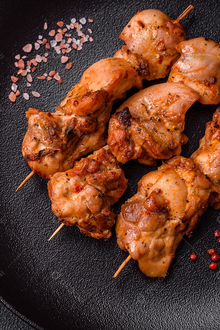 Delicioso frango fresco e suculento ou kebab de porco em espetos com sal e especiarias sobre um fundo escuro de concreto