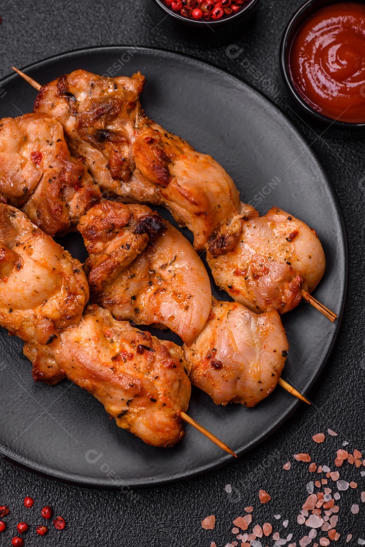 Delicioso frango fresco e suculento ou kebab de porco em espetos com sal e especiarias sobre um fundo escuro de concreto