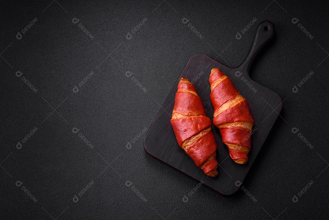 Delicioso croissant vermelho crocante e doce com recheio de creme sobre fundo de concreto texturizado escuro