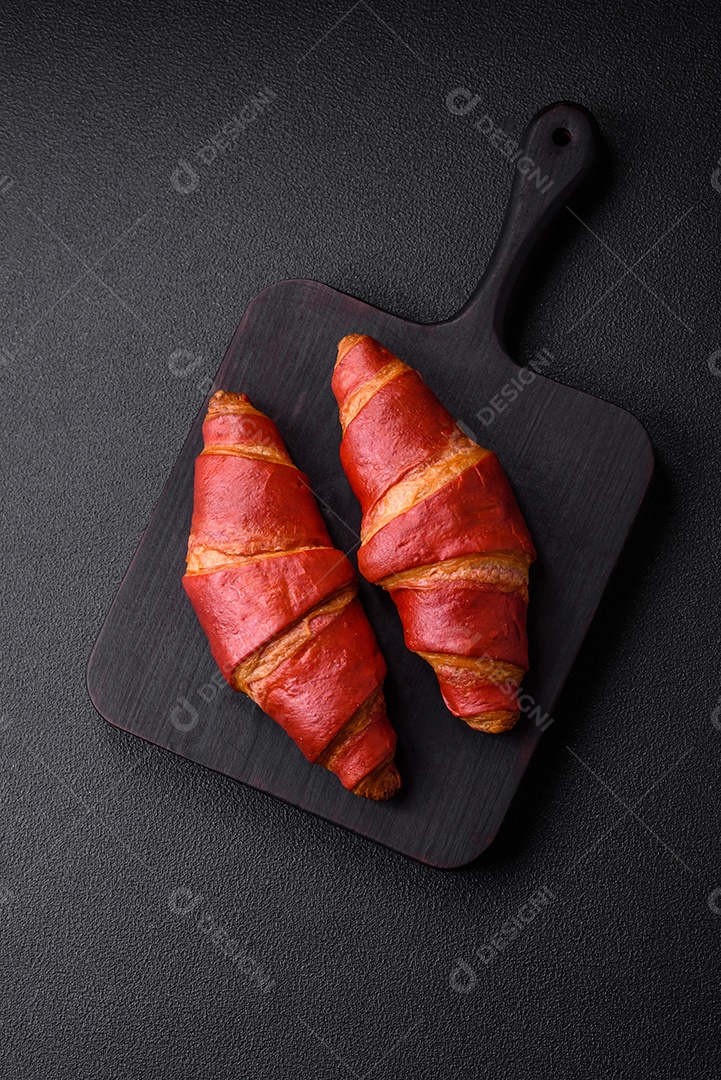 Delicioso croissant vermelho crocante e doce com recheio de creme sobre fundo de concreto texturizado escuro