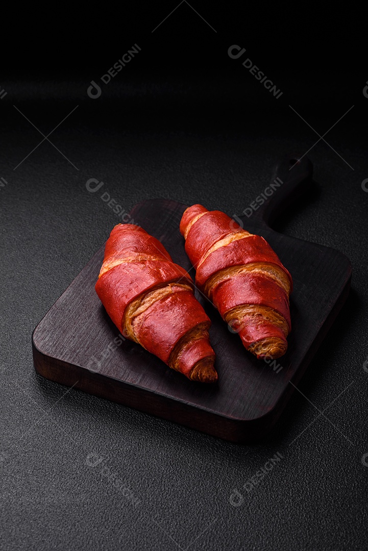 Delicioso croissant vermelho crocante e doce com recheio de creme sobre fundo de concreto texturizado escuro