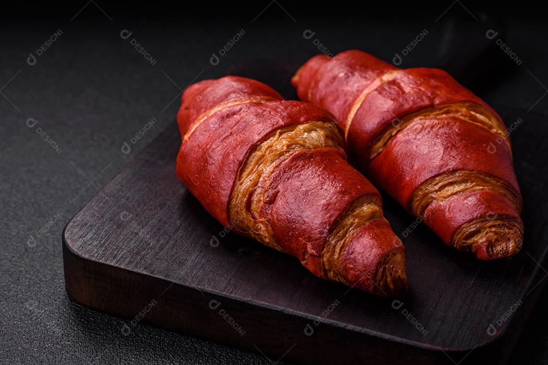 Delicioso croissant vermelho crocante e doce com recheio de creme sobre fundo de concreto texturizado escuro