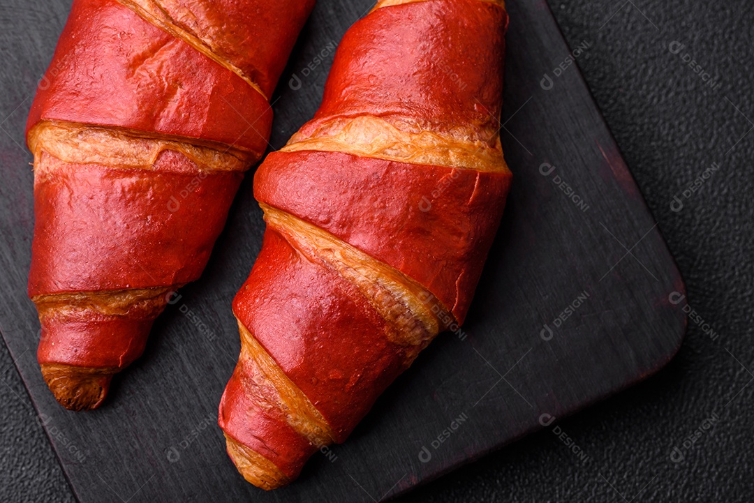 Delicioso croissant vermelho crocante e doce com recheio de creme sobre fundo de concreto texturizado escuro