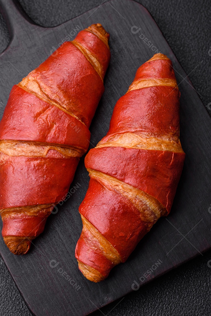 Delicioso croissant vermelho crocante e doce com recheio de creme sobre fundo de concreto texturizado escuro