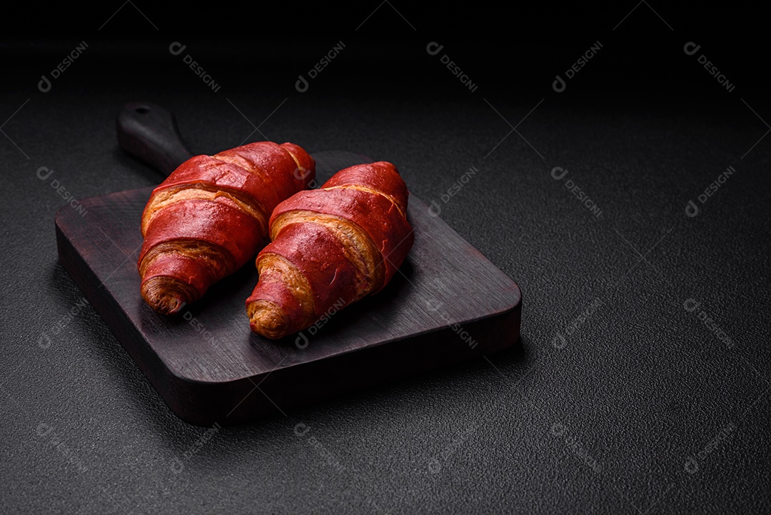 Delicioso croissant vermelho crocante e doce com recheio de creme sobre fundo de concreto texturizado escuro