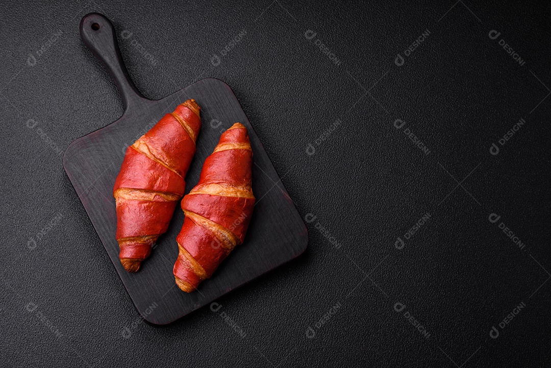 Delicioso croissant vermelho crocante e doce com recheio de creme sobre fundo de concreto texturizado escuro