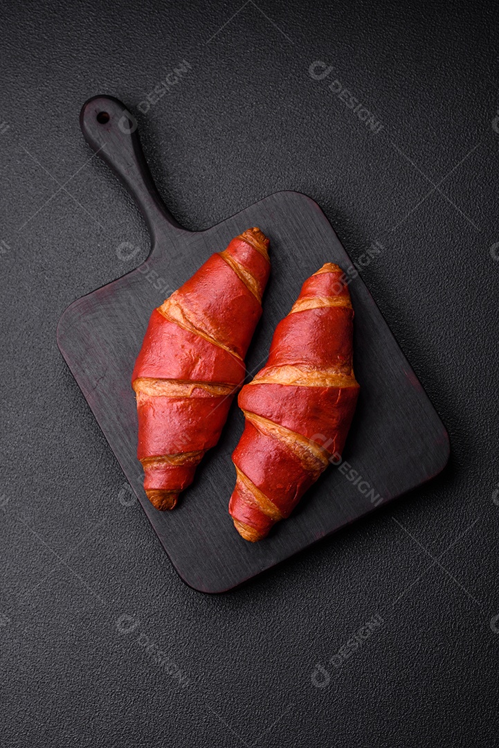 Delicioso croissant vermelho crocante e doce com recheio de creme sobre fundo de concreto texturizado escuro