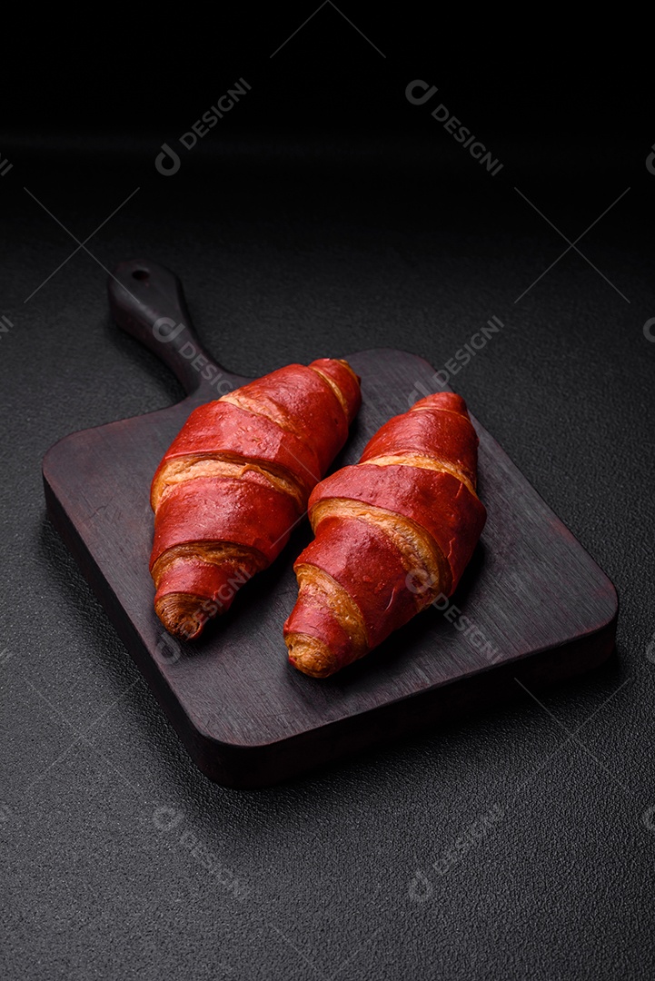 Delicioso croissant vermelho crocante e doce com recheio de creme sobre fundo de concreto texturizado escuro