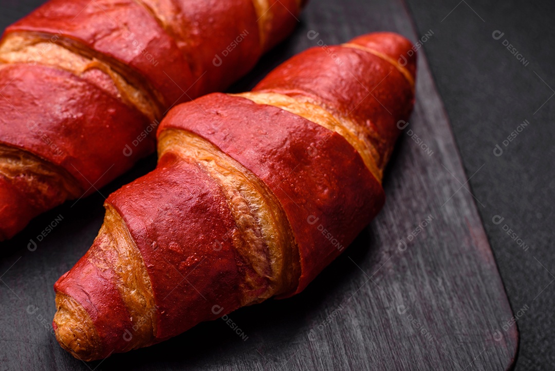 Delicioso croissant vermelho crocante e doce com recheio de creme sobre fundo de concreto texturizado escuro