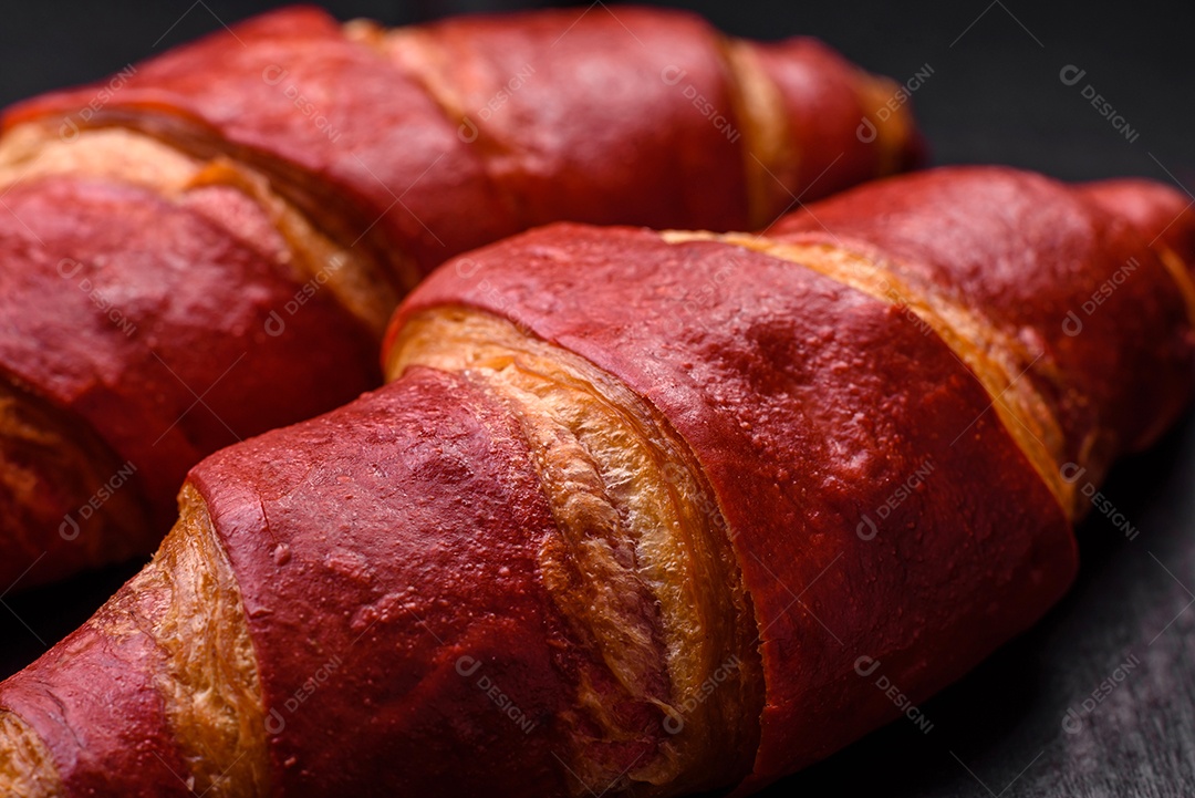 Delicioso croissant vermelho crocante e doce com recheio de creme sobre fundo de concreto texturizado escuro