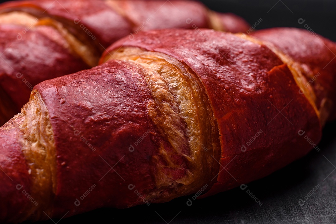 Delicioso croissant vermelho crocante e doce com recheio de creme sobre fundo de concreto texturizado escuro