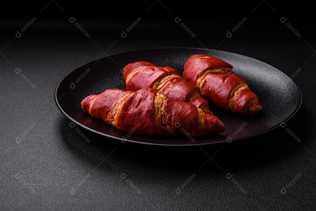 Delicioso croissant vermelho crocante e doce com recheio de creme sobre fundo de concreto texturizado escuro