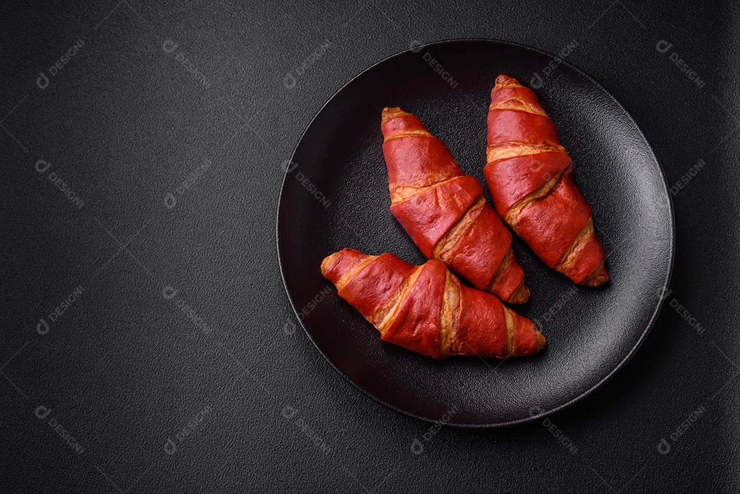 Delicioso croissant vermelho crocante e doce com recheio de creme sobre fundo de concreto texturizado escuro