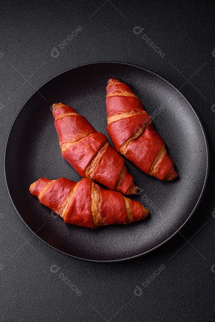 Delicioso croissant vermelho crocante e doce com recheio de creme sobre fundo de concreto texturizado escuro