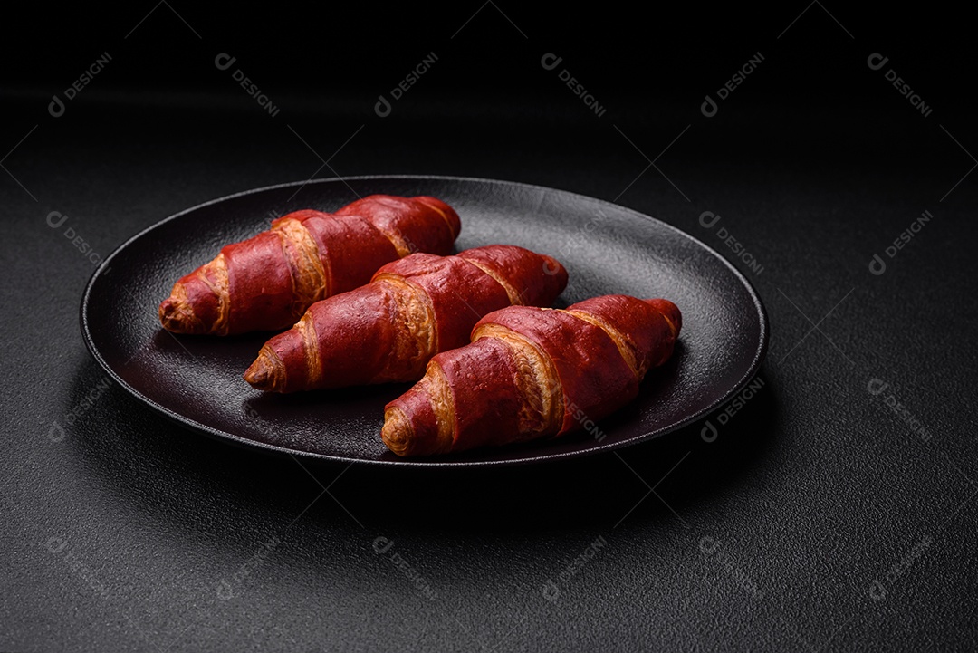 Delicioso croissant vermelho crocante e doce com recheio de creme sobre fundo de concreto texturizado escuro