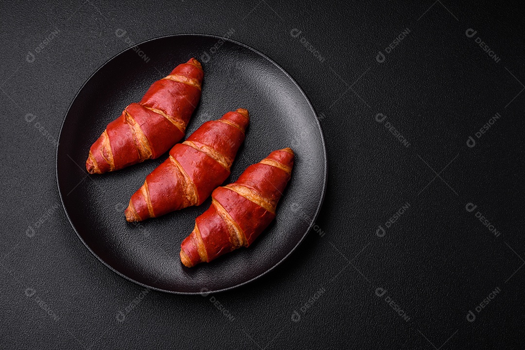 Delicioso croissant vermelho crocante e doce com recheio de creme sobre fundo de concreto texturizado escuro