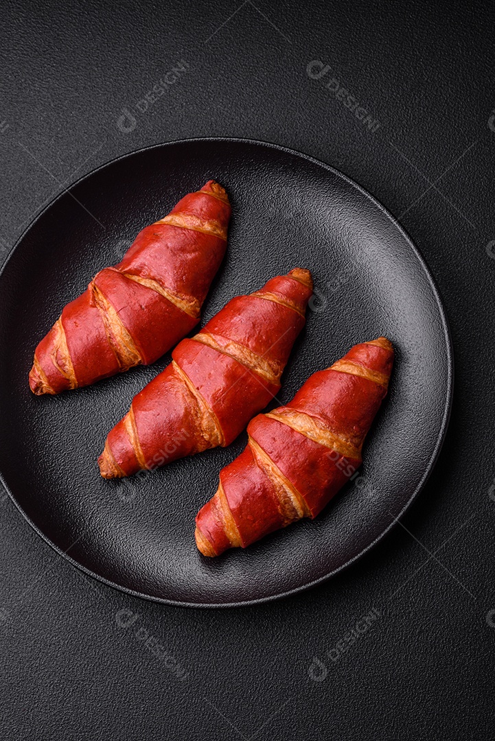 Delicioso croissant vermelho crocante e doce com recheio de creme sobre fundo de concreto texturizado escuro